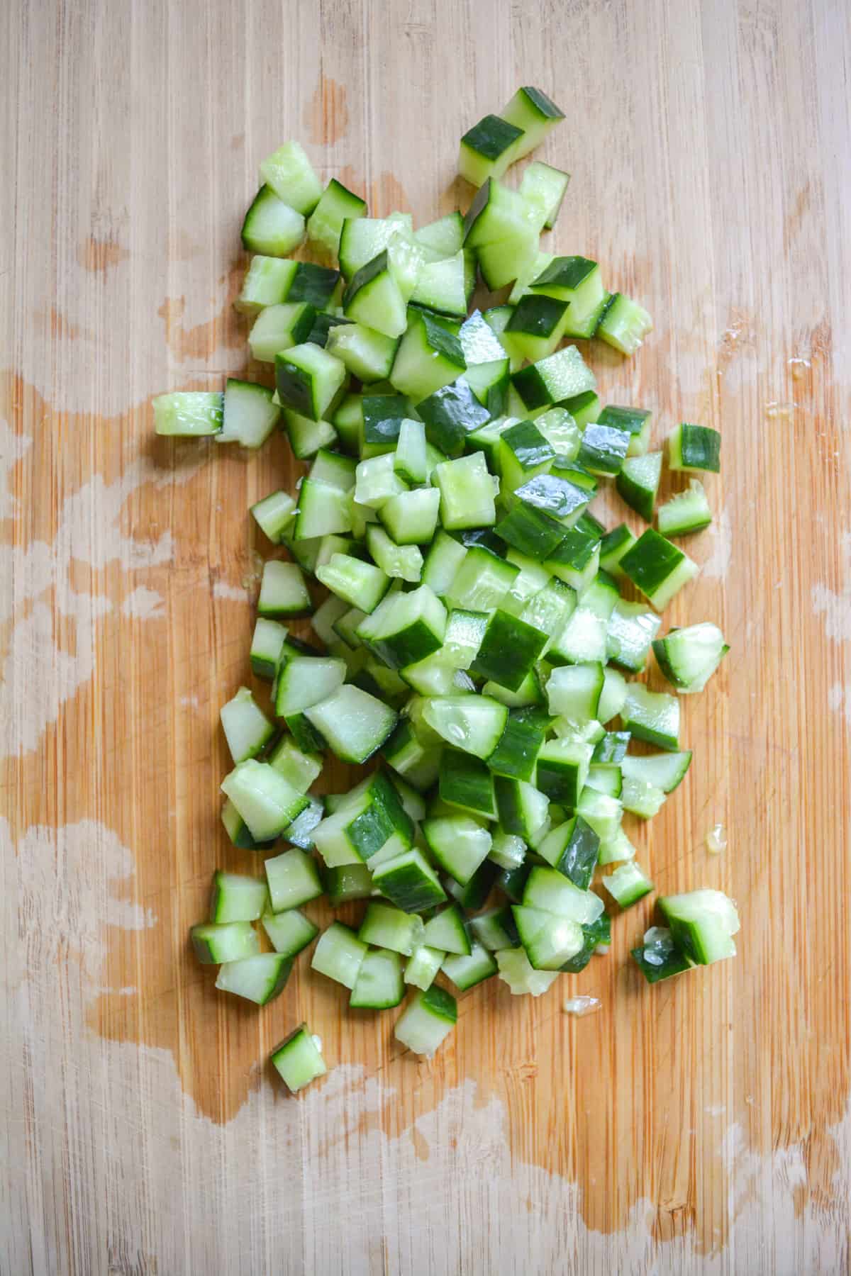 Diced english cucumber on a wooden cutting board.