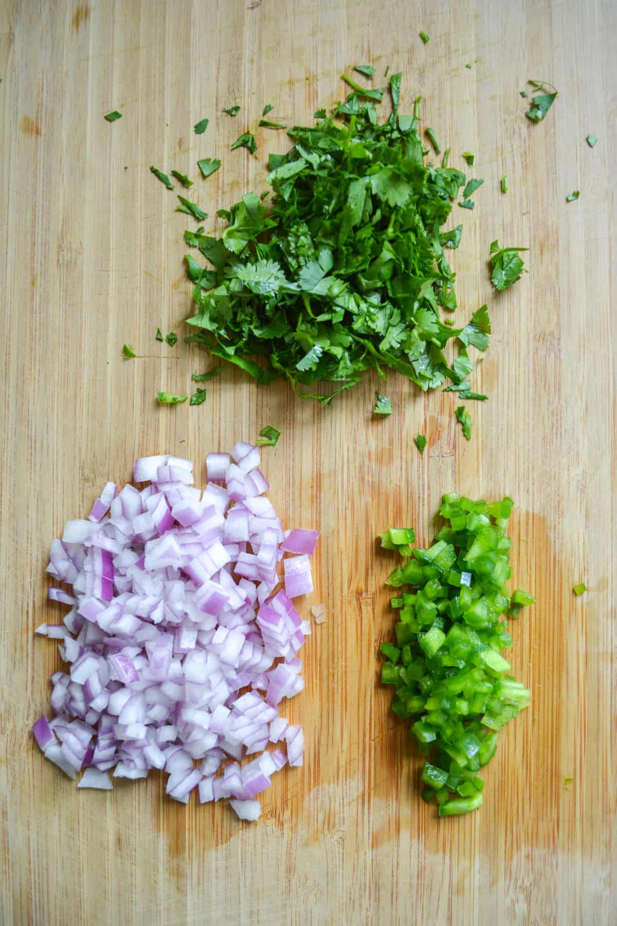 Finely chopped onion, jalapeño and cilantro on a cutting board.