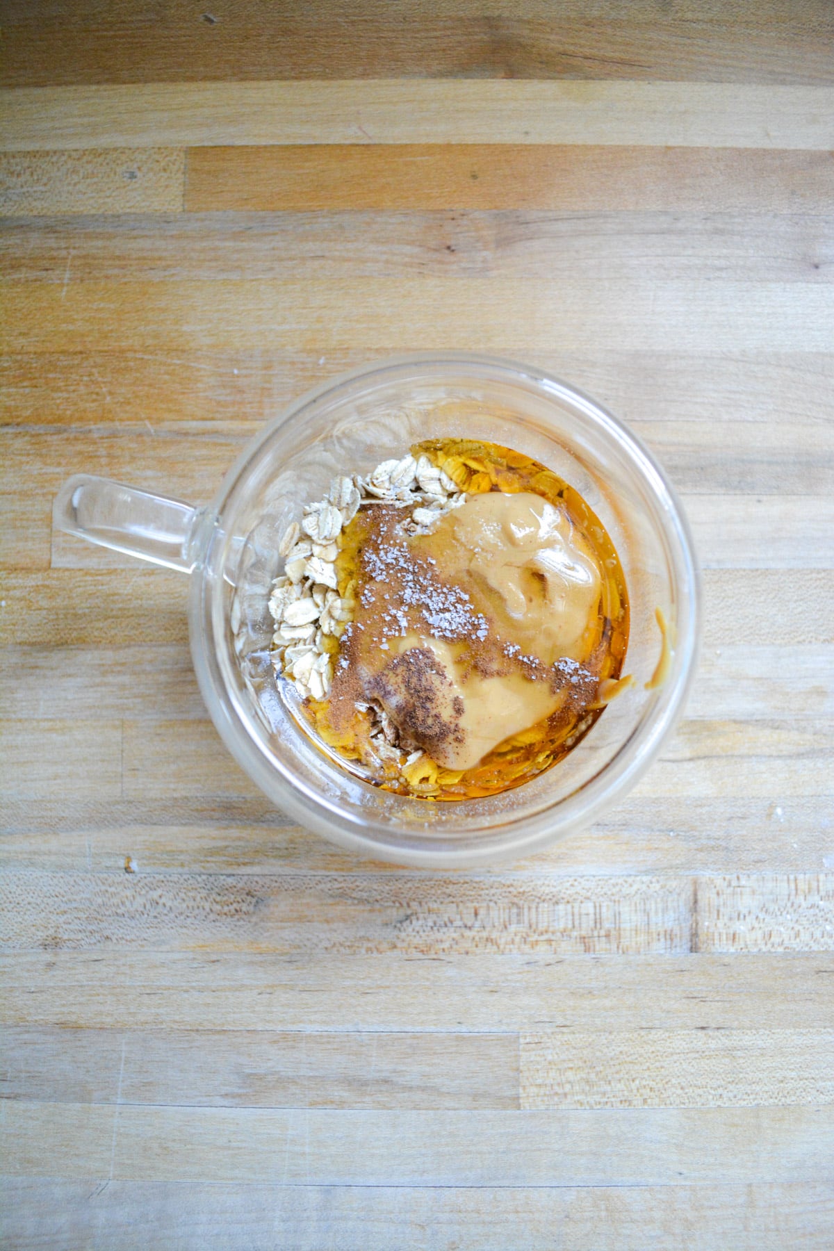Rolled oats, nut butter and maple syrup in a small glass cup.