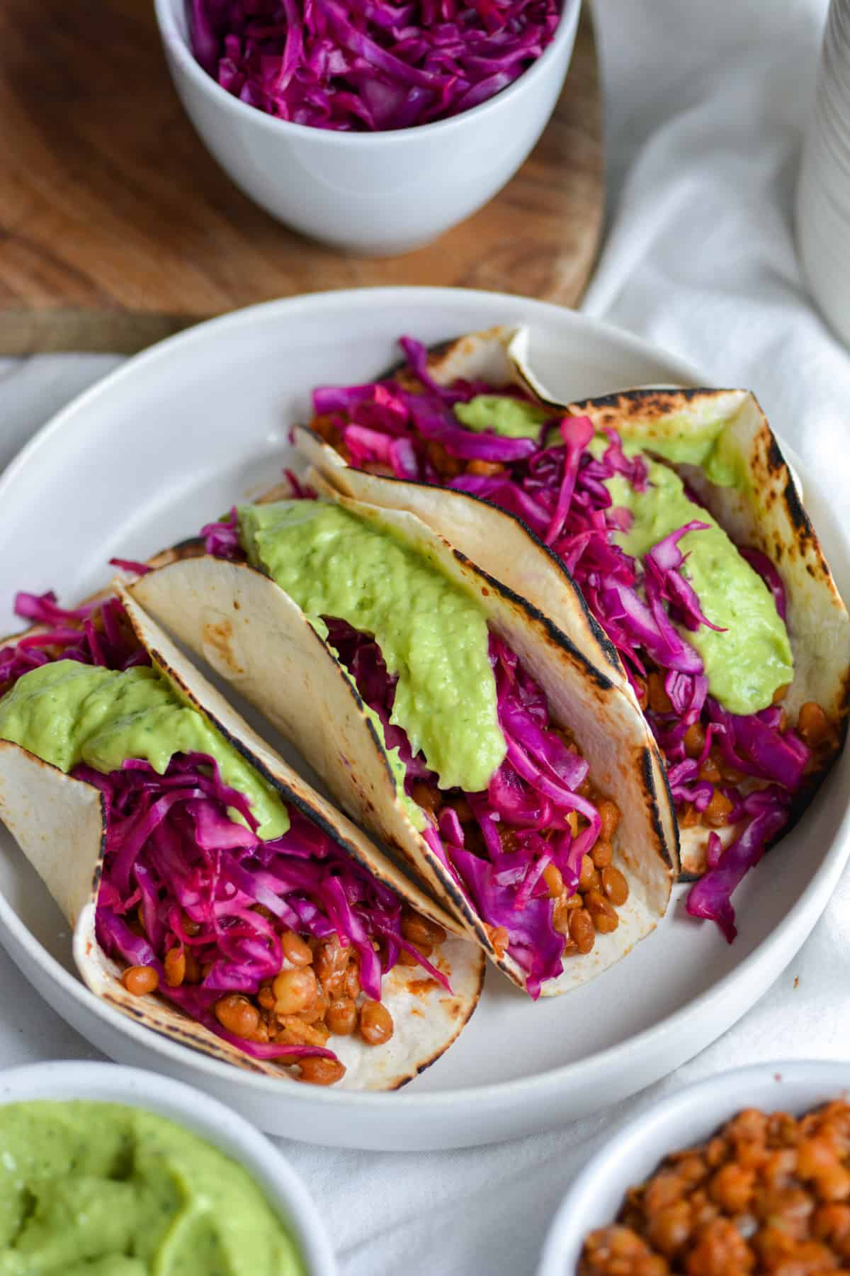 Vegan Lentil Tacos in a bowl topped with red cabbage slaw and avocado crema.