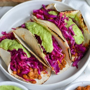 3 Vegan Lentil Tacos topped with red cabbage slaw and avocado crema in a shallow bowl.