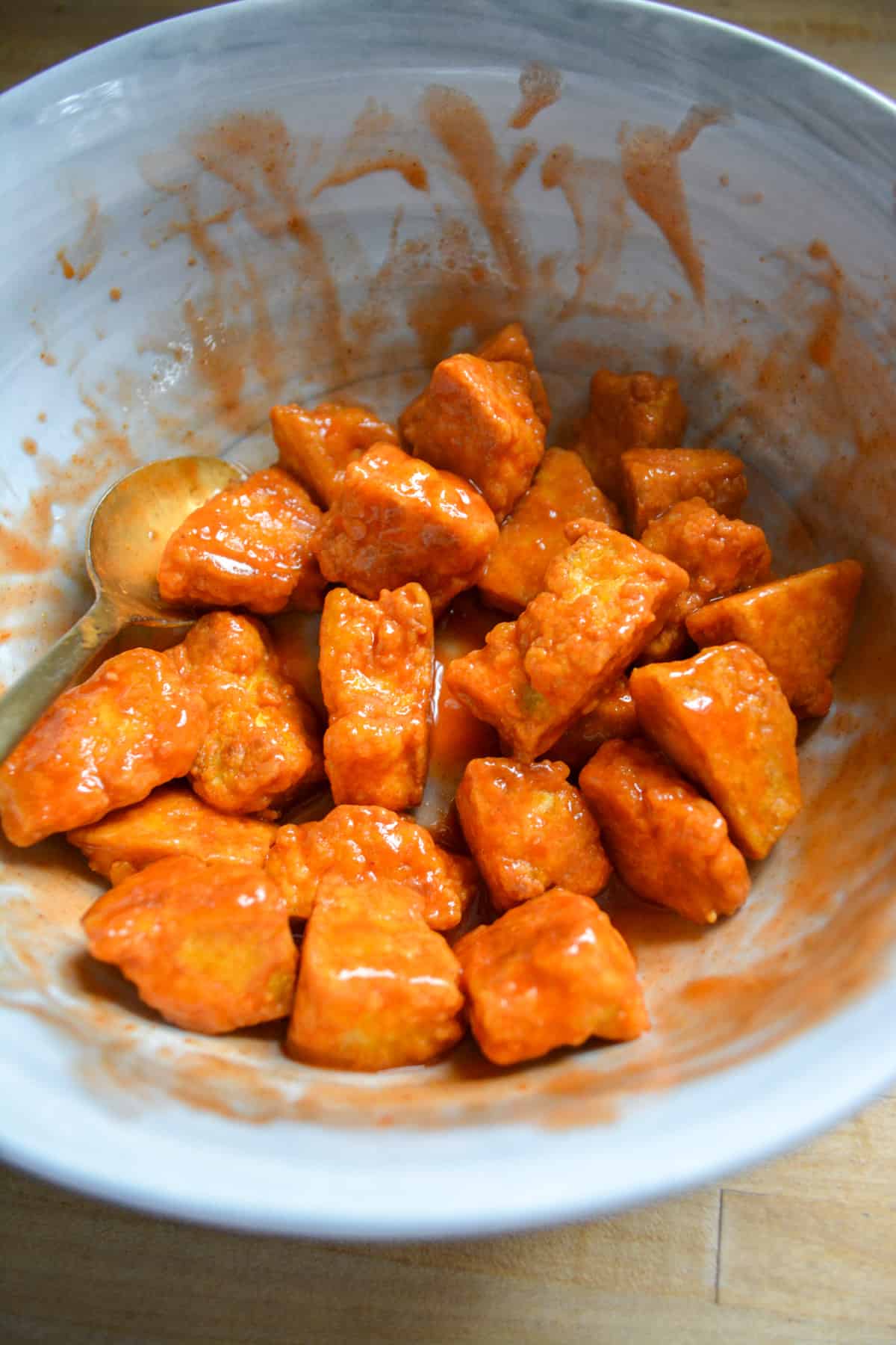 Crispy baked tofu tossed with buffalo sauce in a mixing bowl.
