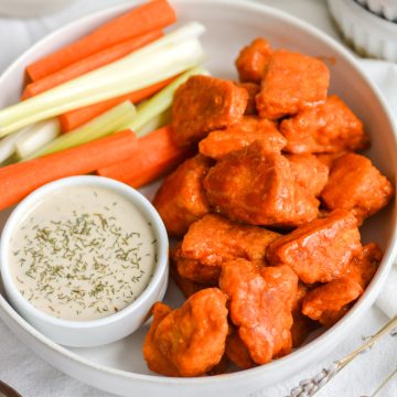 Buffalo Tofu Chicken Wings in a bowl with a small container of ranch dressing and some carrot and celery sticks.