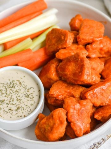 Buffalo Tofu Chicken Wings in a bowl with a small container of ranch dressing and some carrot and celery sticks.