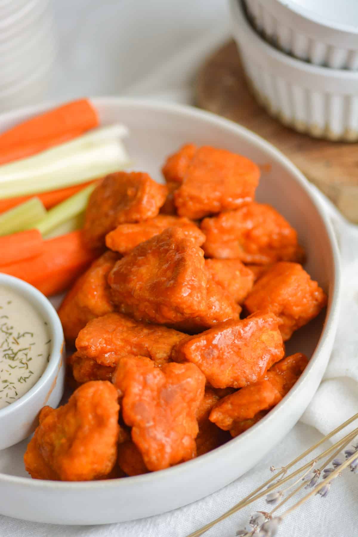 Buffalo Tofu Wings in a white bowl next to a small container of ranch and carrot carrot and celery sticks toward the back.