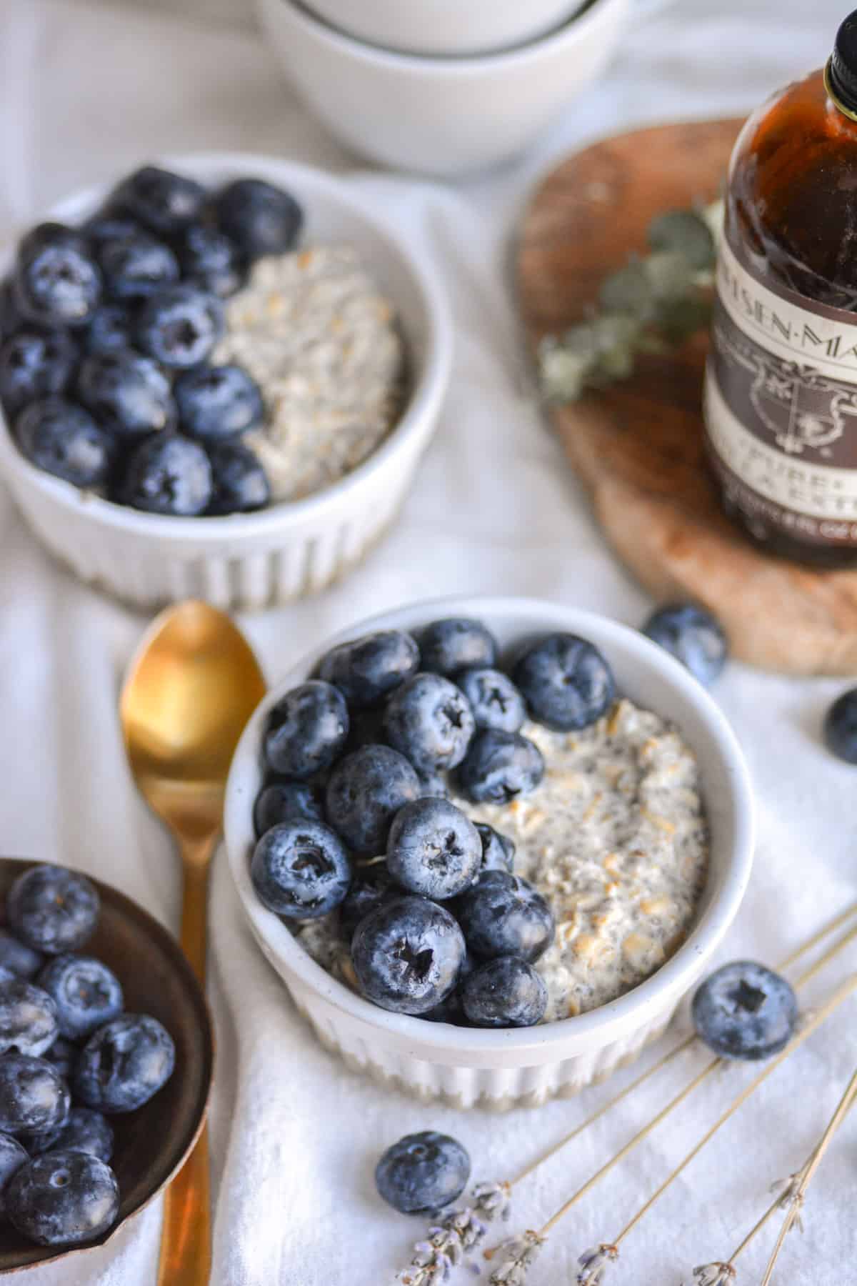 Vegan Vanilla Overnight Oats in two ramekins toped with blueberries with a gold spoon to the left.