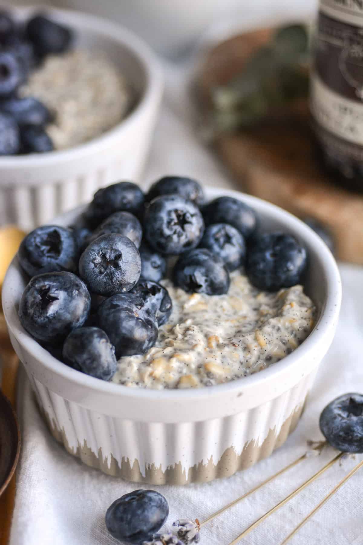 Vegan Vanilla Overnight Oats in a ramekin topped with blueberries on a white cloth.