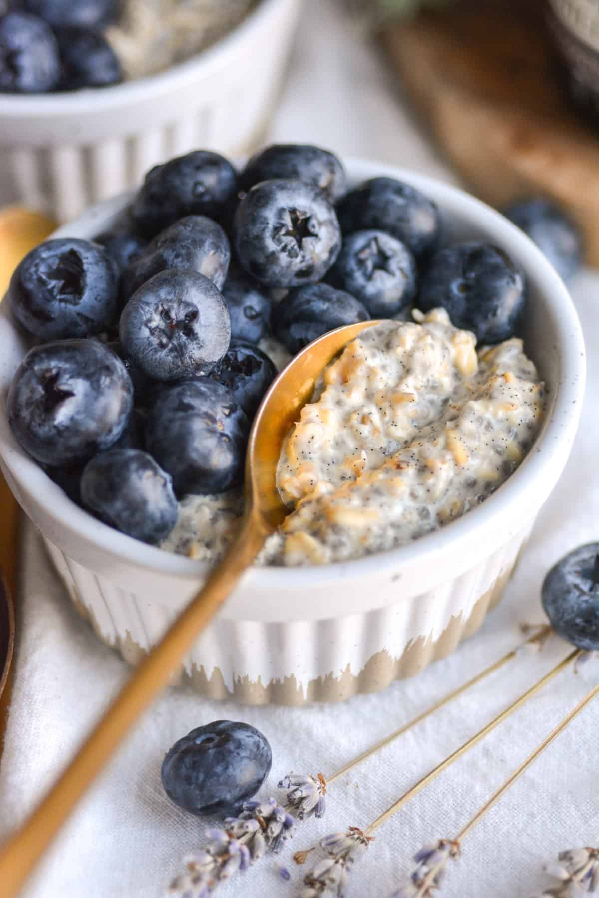 Vegan Vanilla Overnight Oats in a ramekin topped with blueberries with. gold spoon inside of the oats.