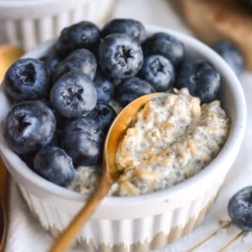 Vegan Vanilla Overnight Oats in a ramekin topped with blueberries with a gold spoon inside.