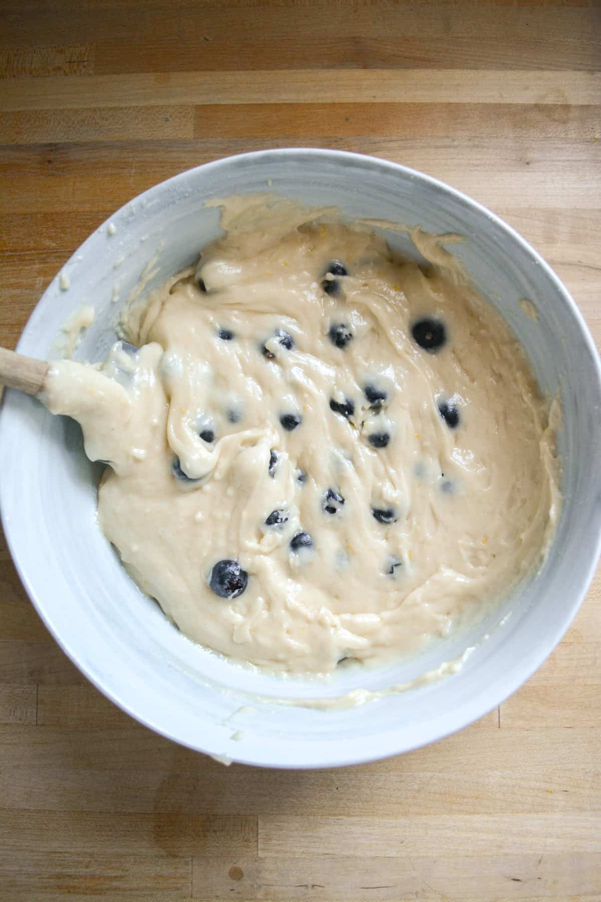 Fresh blueberries folded into the cake batter in a large bowl with a spatula off to the left.