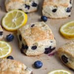 Vegan Blueberry scones on a baking sheet with lemon slices and blueberries scattered around.