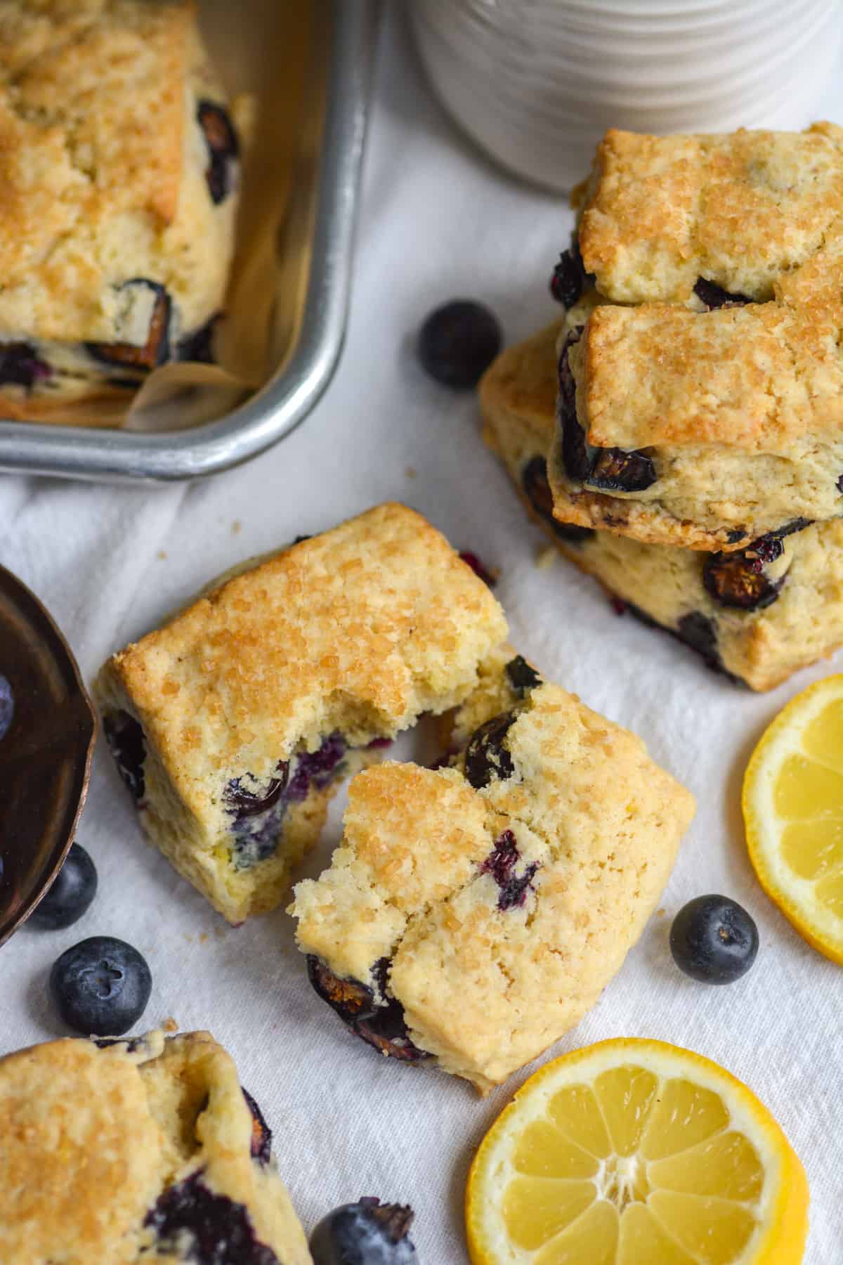 Vegan Blueberry scone broken in half on a surface with blueberries and lemon slices in the scene.