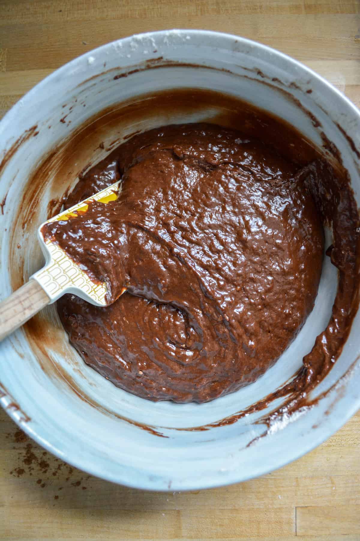 Dry ingredients folded into the batter in a mixing bowl with a spatula toward the left.