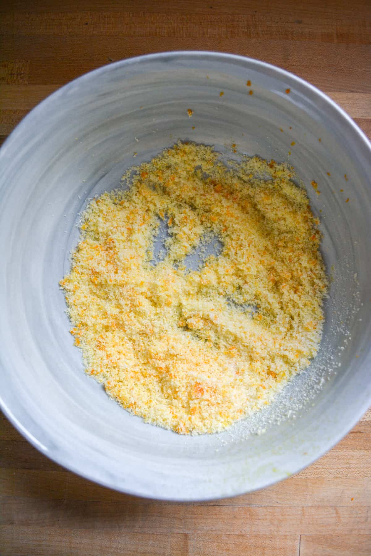 Orange zest rubbed into granulated sugar in a mixing bowl.