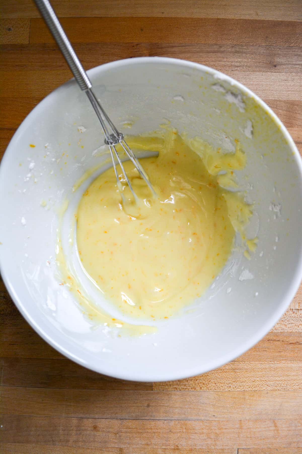 Vegan orange glaze in a small bowl with a small whisk in it.