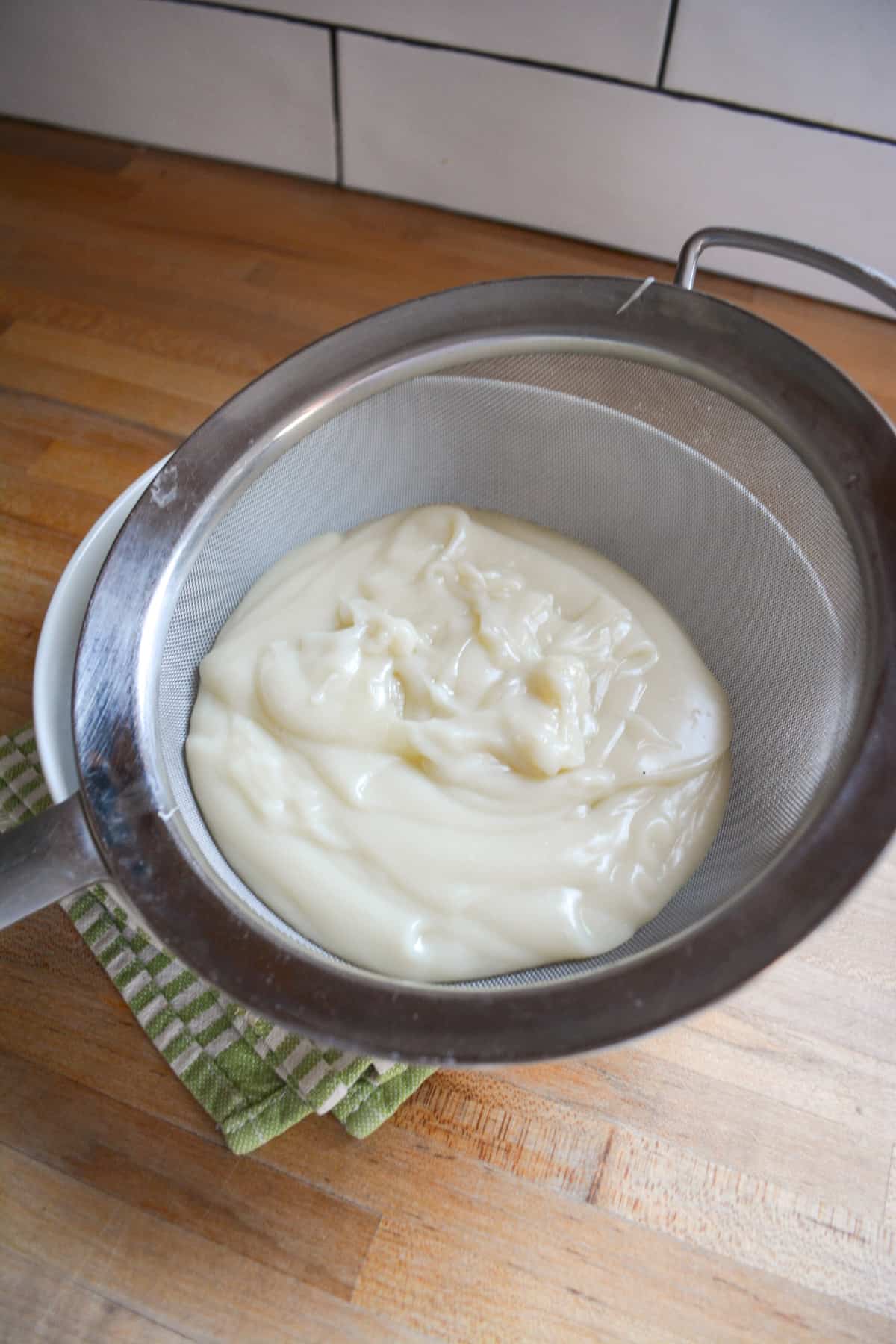 Dairy free custard being strained through a fine mesh strainer into a bowl.