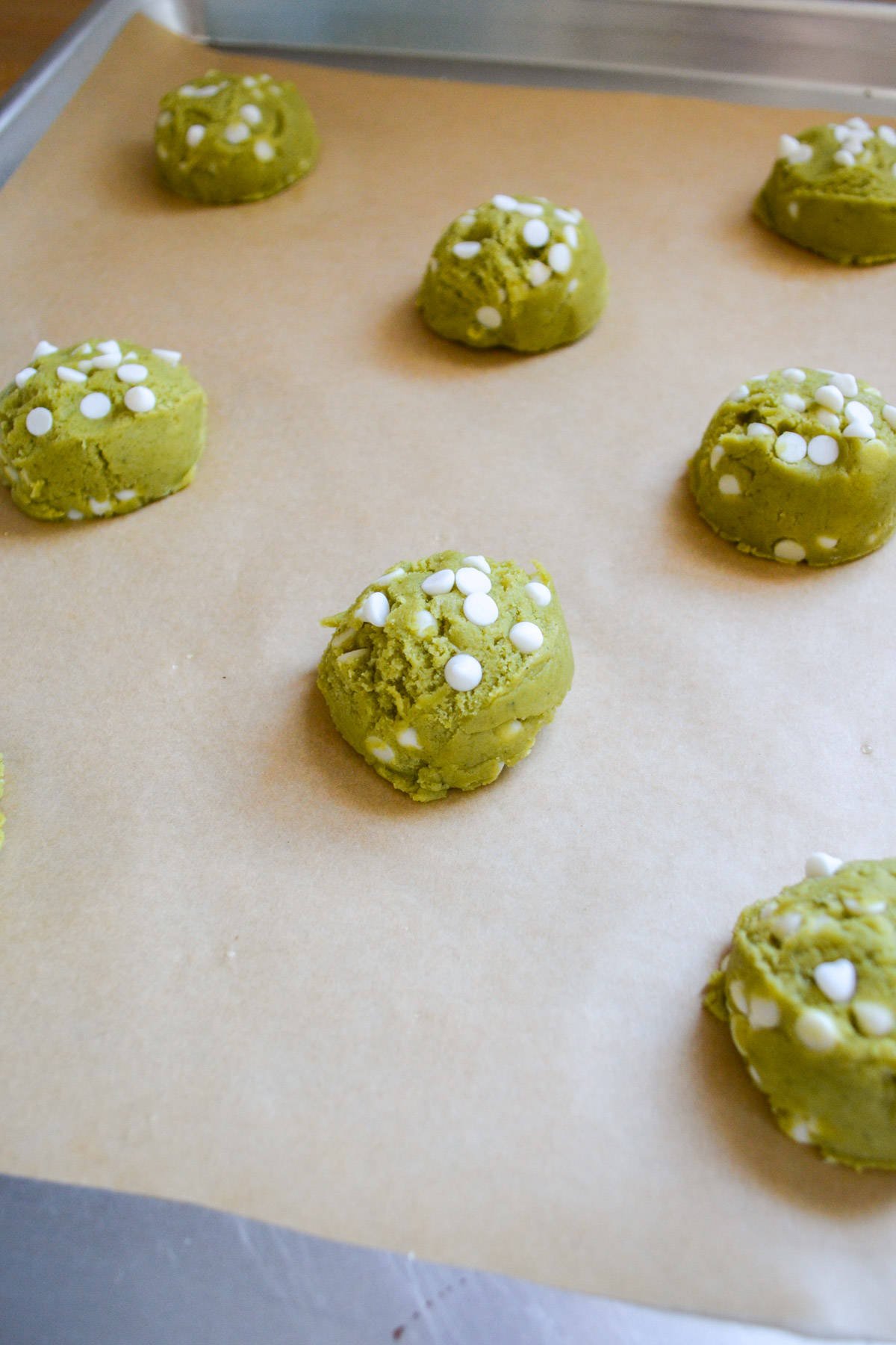 Scooped matcha cookies on a parchment lined baking sheet.