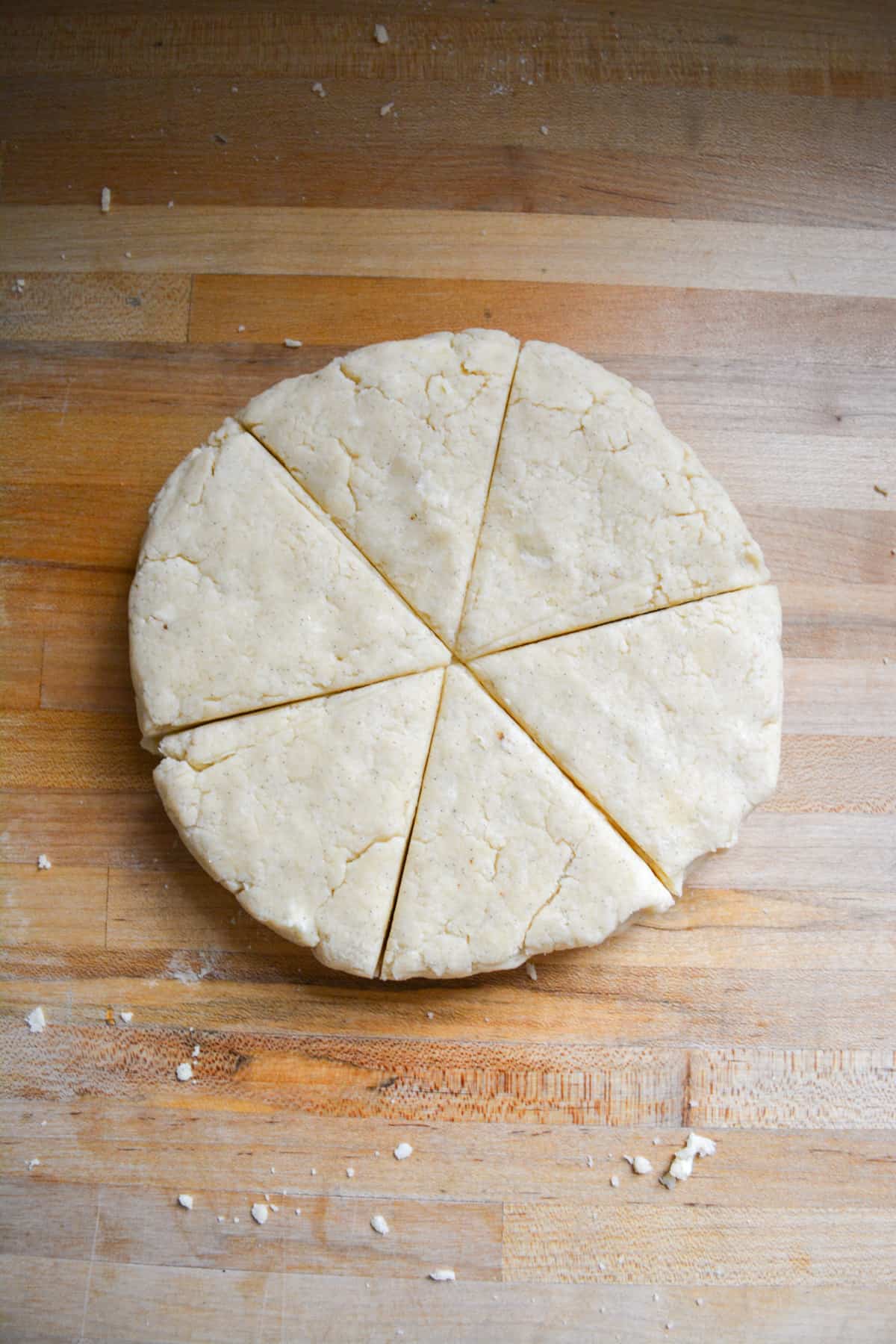 Vegan Scone dough pressed into a circle on a wooden surface and cut into 6 triangles.
