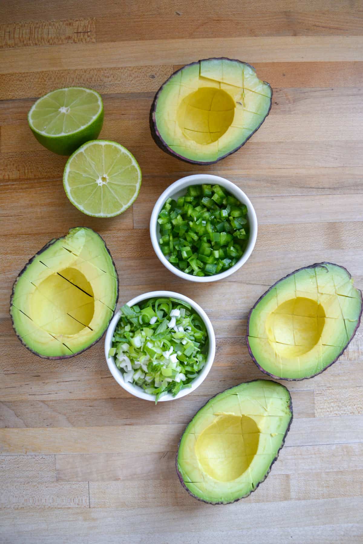Chopped jalapeño and spring onion in small bowls next to halved avocados.