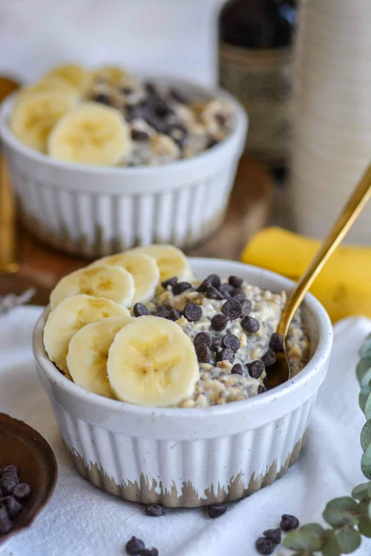 Banana Chocolate Chip Overnight Oats in a ramekin with banana slices and mini chocolate chips on top and a spoon coming out of the right of the ramekin.