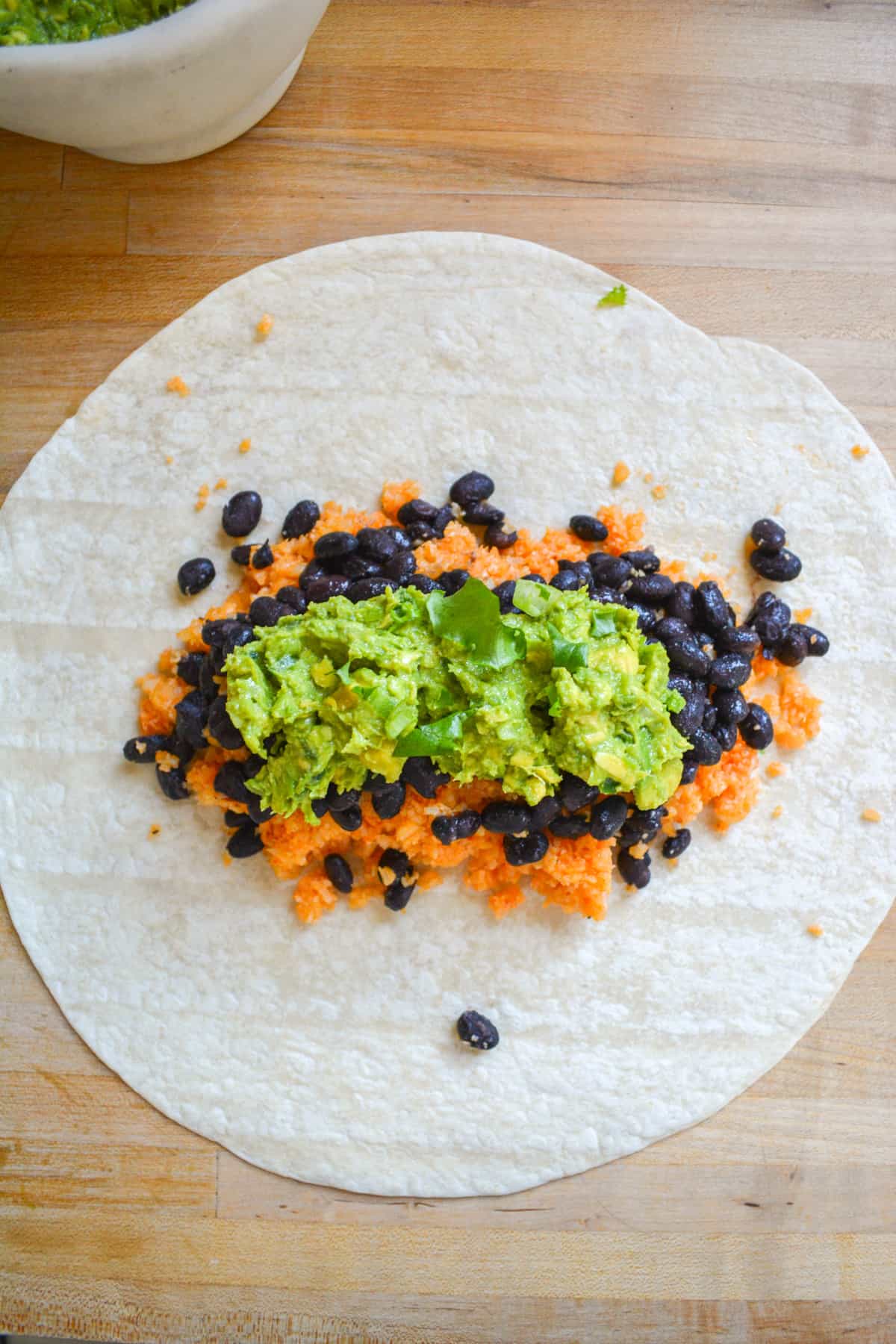 Large tortilla with buffalo cauliflower rice black beans and guacamole on it.