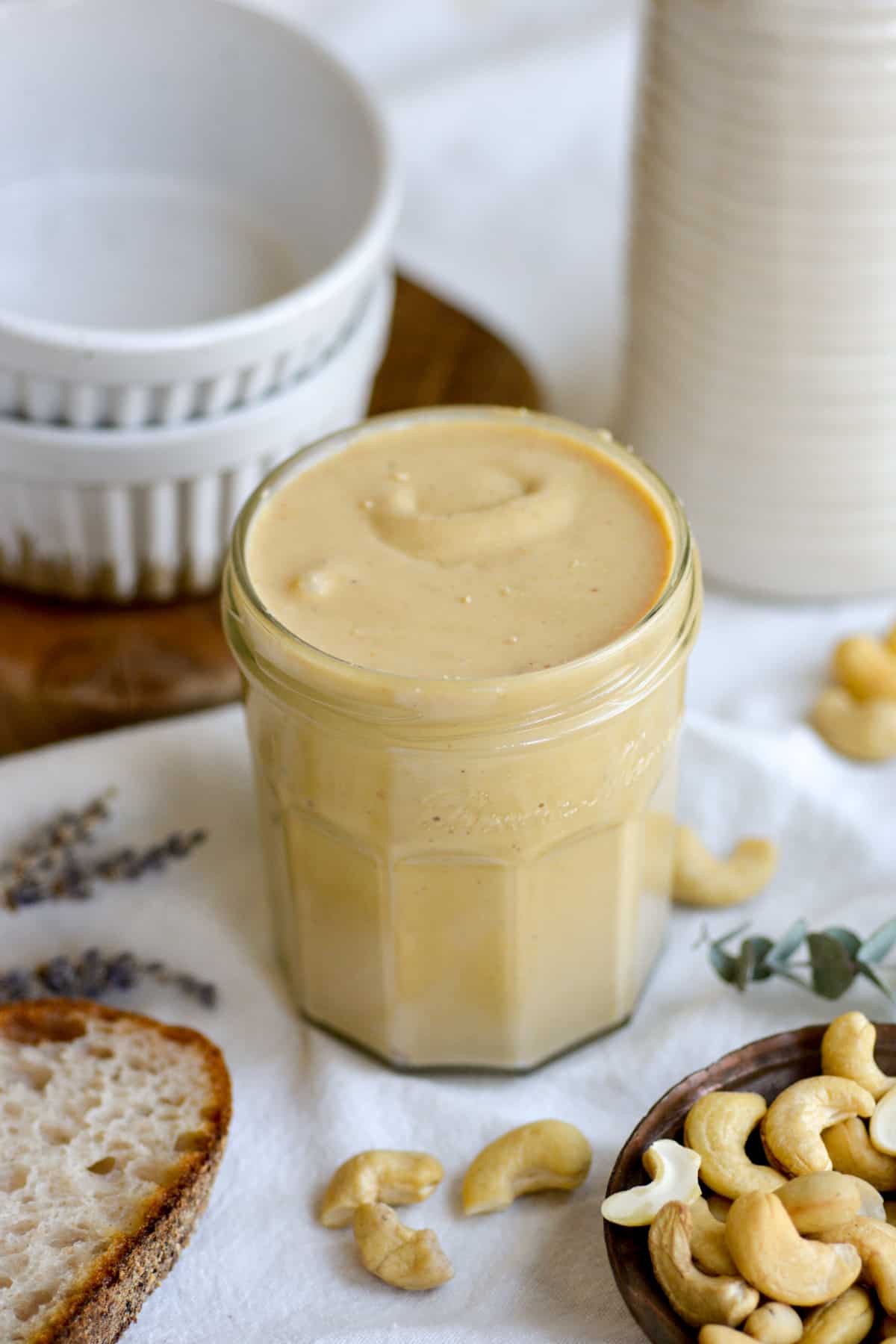 Cashew butter in a glass jar with cashews scattered around the scene.