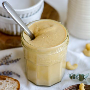 Cashew butter in a glass jar with a knife sticking out of it.