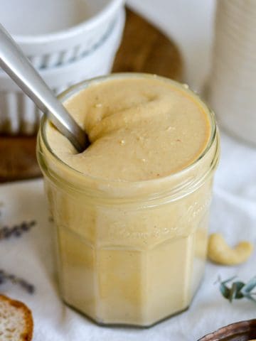 Cashew butter in a glass jar with a knife sticking out of it.
