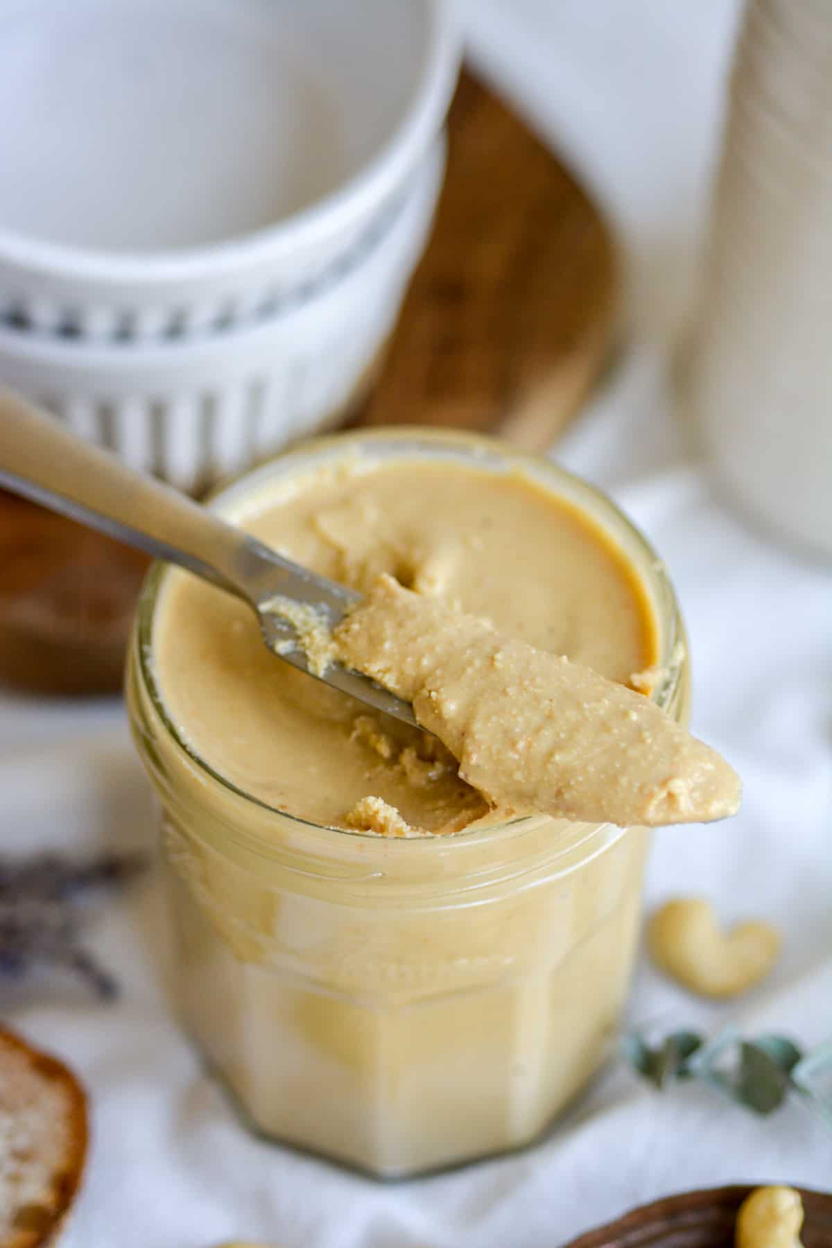 A knife with cashew butter on it laying on top of a jar full of cashew butter.