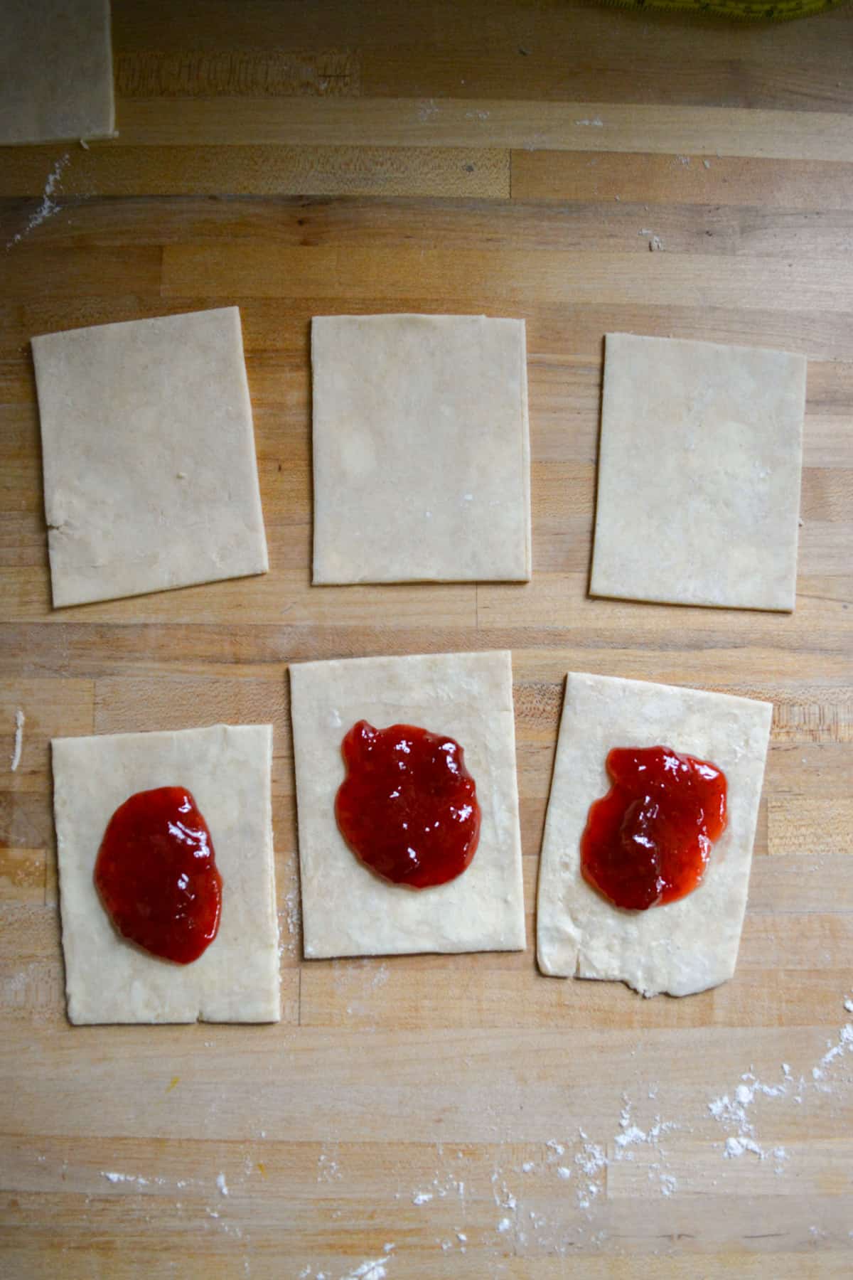 Strawberry jam on 3 pie dough rectangles and 3 rectangles with nothing on them.