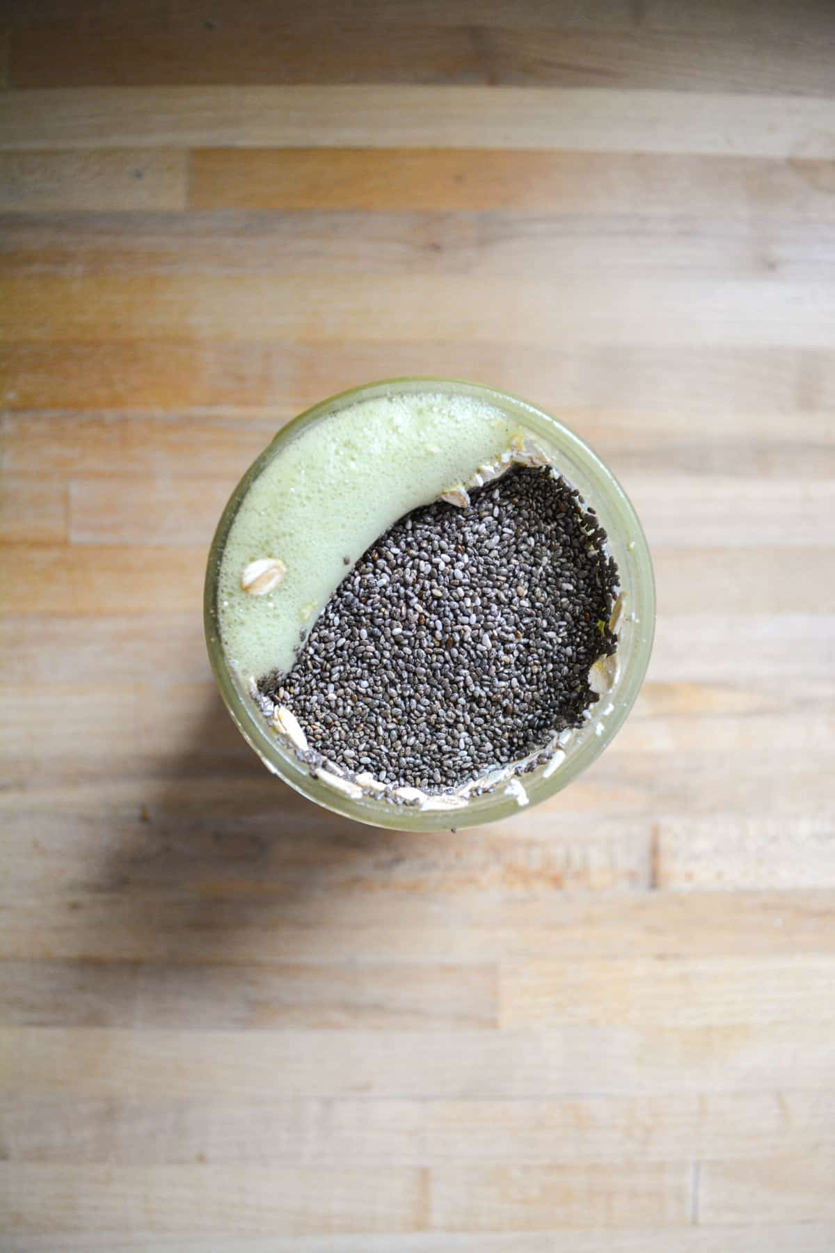 Chia seeds and oats added into the overnight oat liquid ingredients in a glass jar.