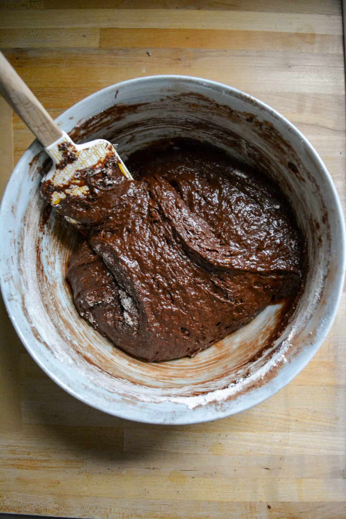 Cocoa powder and flour folded into the mix to form the brownie batter in a large mixing bowl with a rubber spatula to the top left.