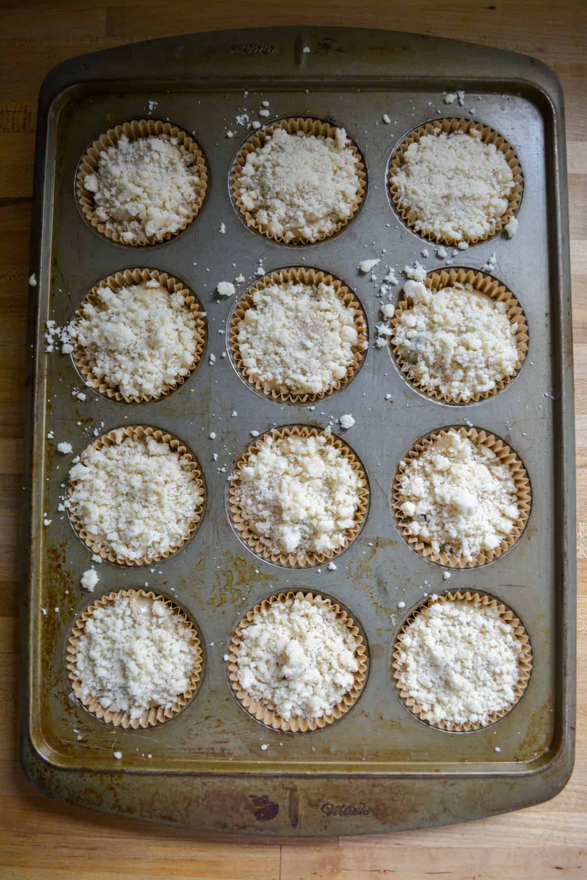 Muffin batter in the muffin tin, topped with crumb topping, ready to bake.