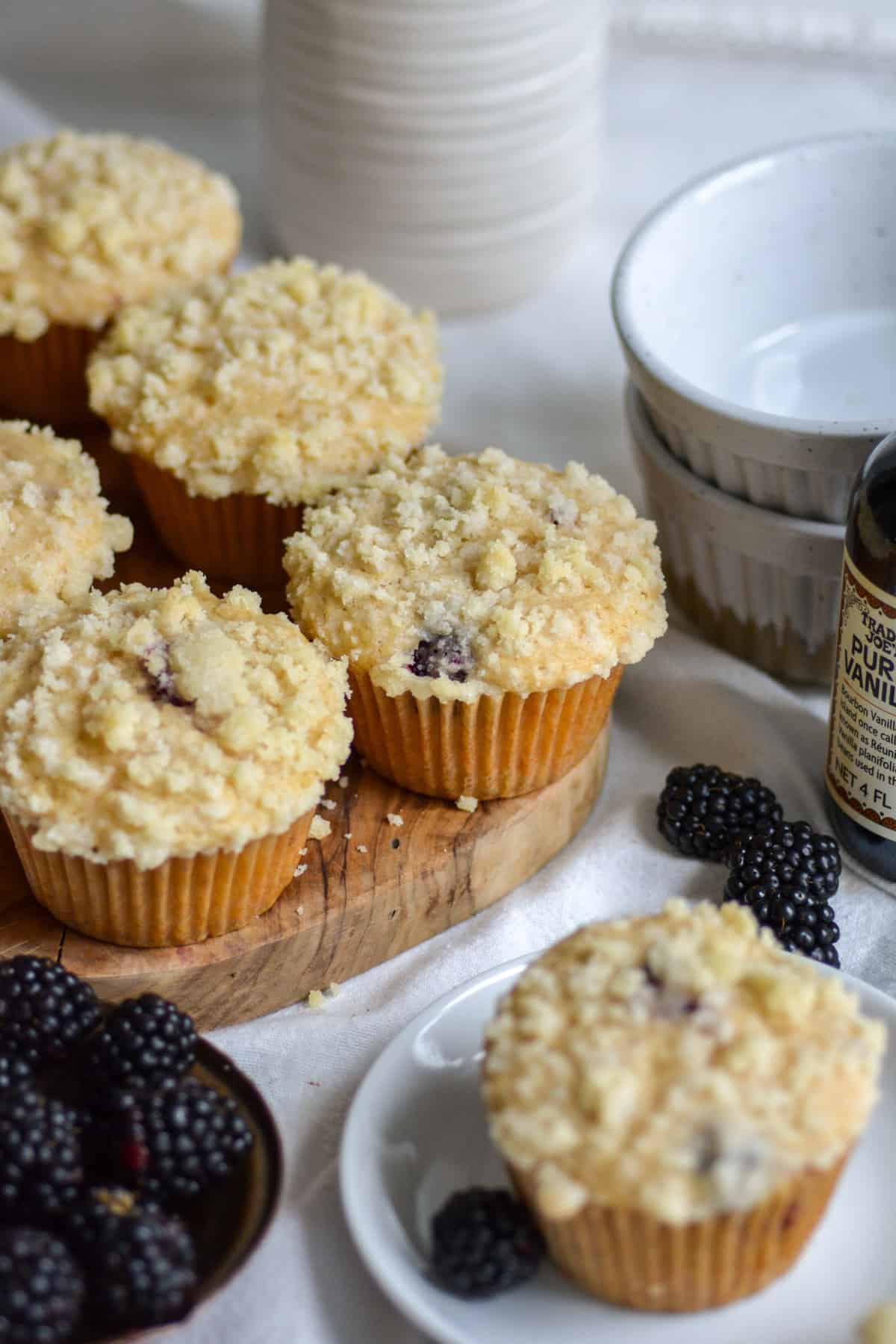 Vegan Blackberry muffins on a small wooden board with a muffin on a plate in the foreground.