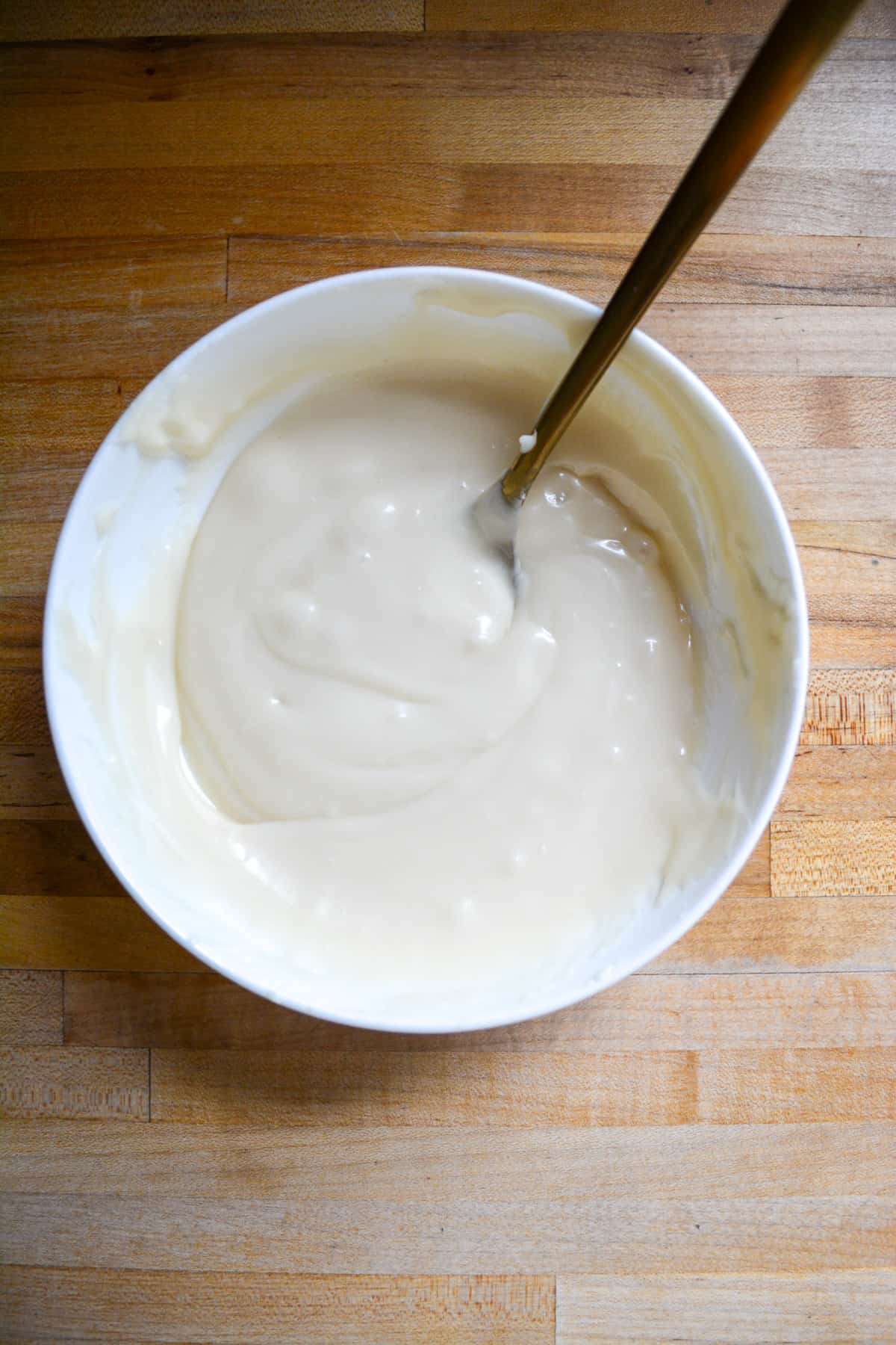 Vegan cream cheese frosting in a medium bowl with a spoon to the right.