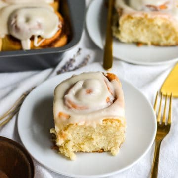 Vegan Cinnamon Roll topped with cream cheese frosting on a small plate with a fork to the right.