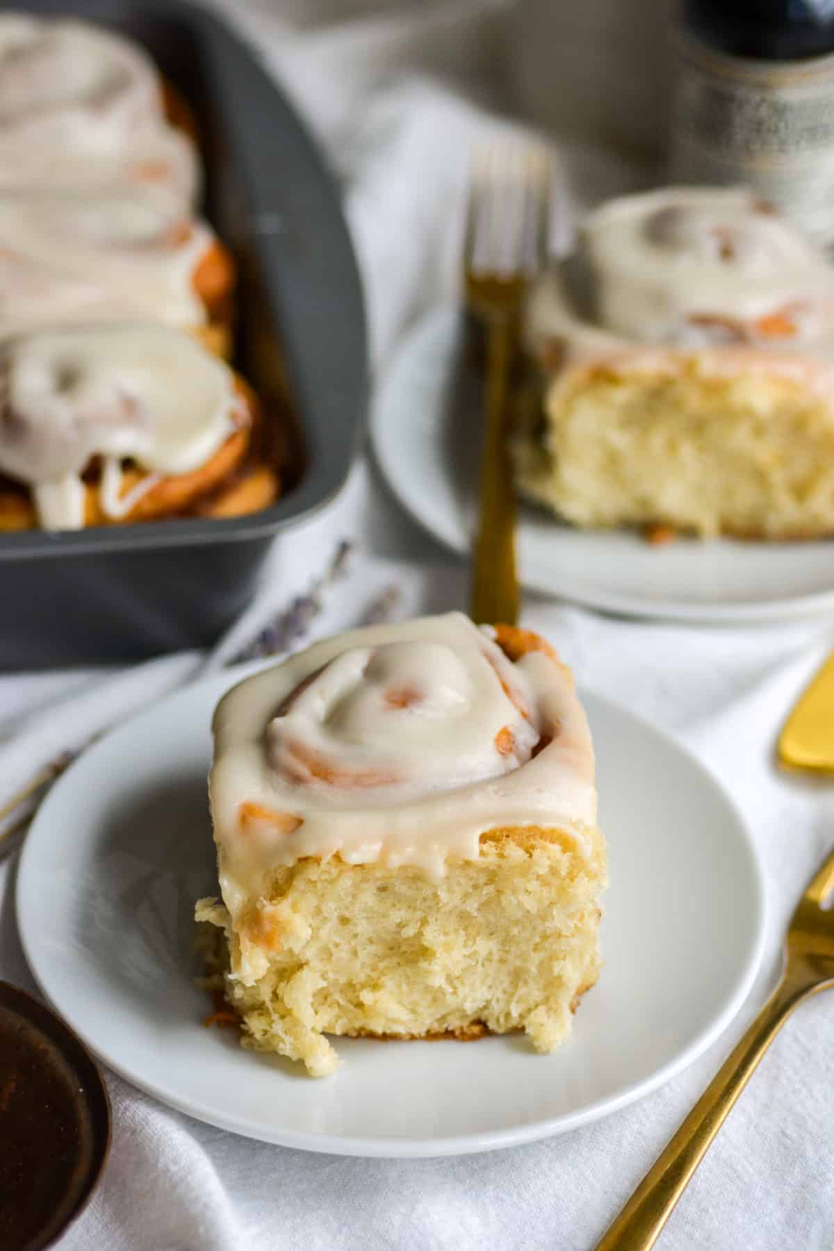 Eggless Vegan Cinnamon Roll with cream cheese frosting on a small plate with more cinnamon rolls in the background.