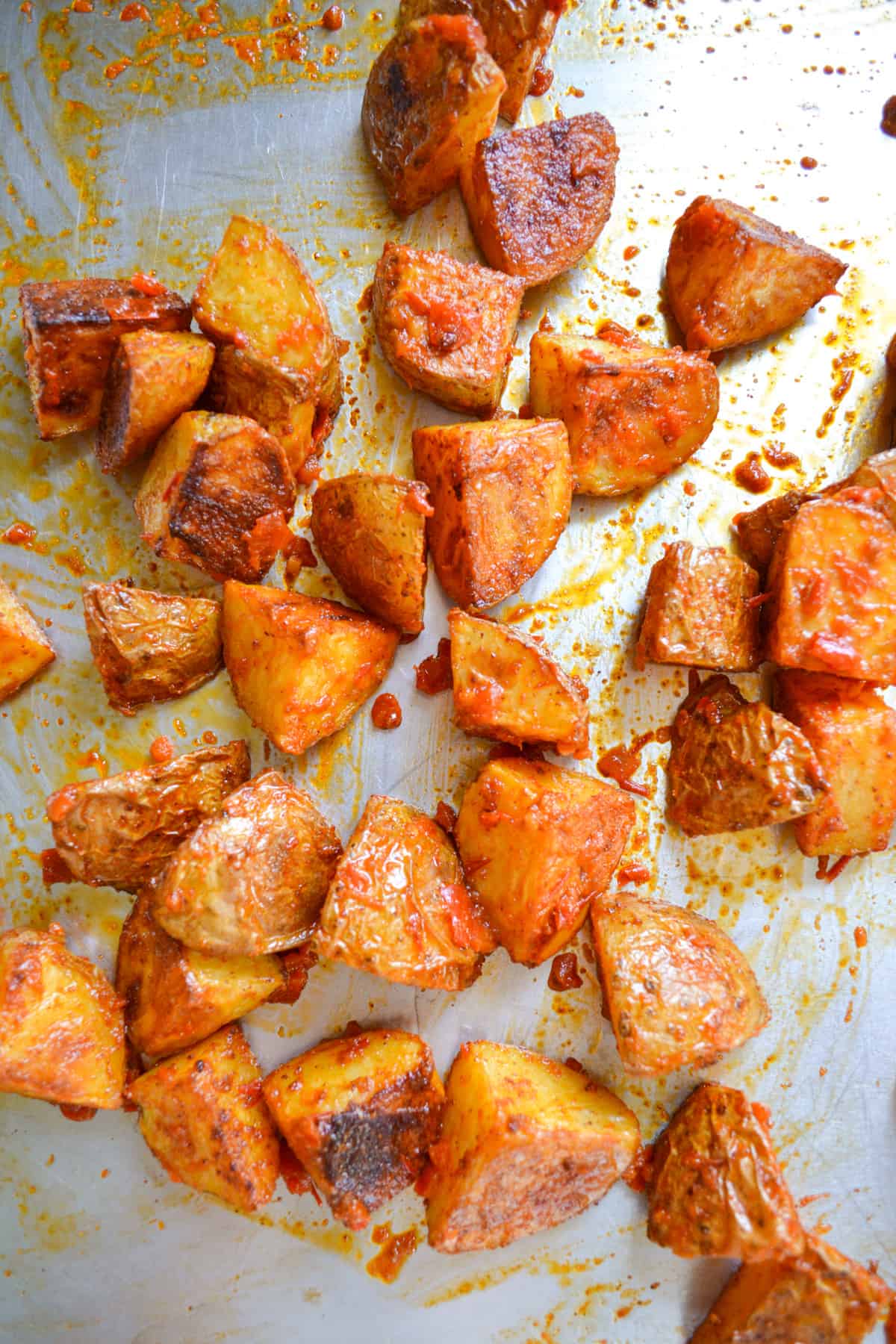 Roasted potatoes tossed with harissa sauce on a baking sheet.
