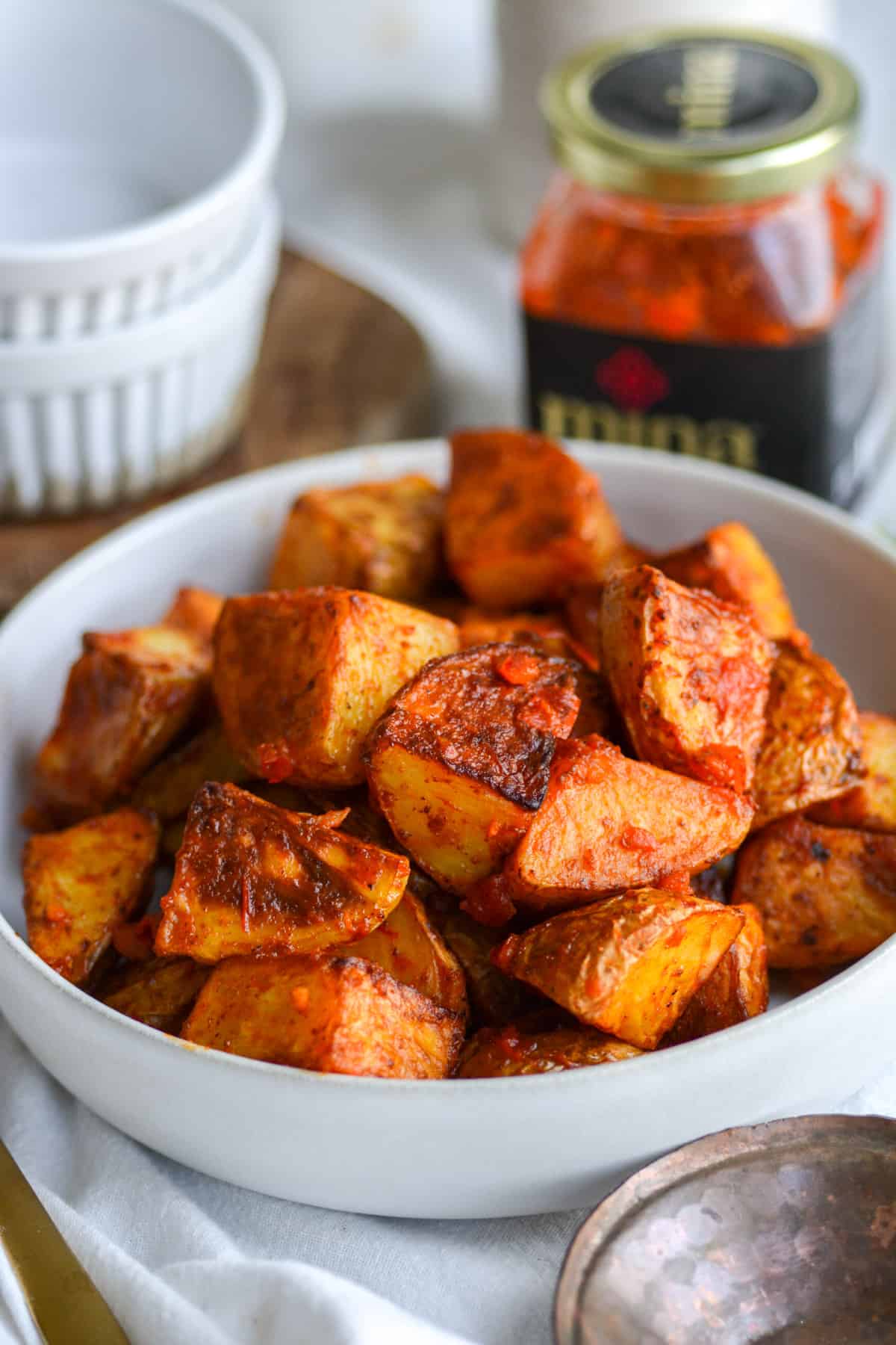 Vegan Spicy Harissa Roasted Potatoes in a shallow bowl with a jar of harissa in the background.