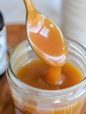 Vegan Salted Caramel Sauce on a spoon pouring into a glass jar.