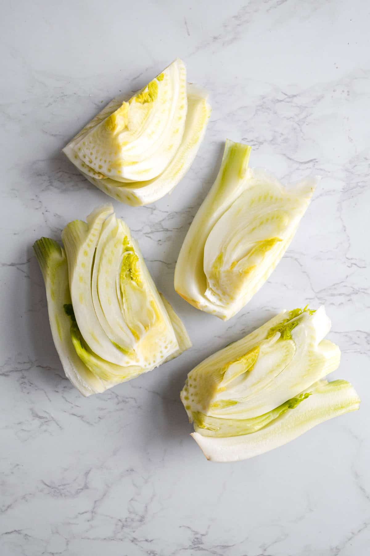Quartered and cored fennel bulb on a marble surface.