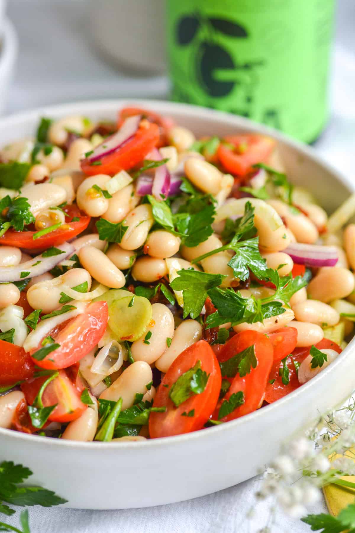 Tuscan cannellini bean salad with tomatoes and parsley in it in a large bowl on a white cloth.