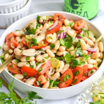 Italian cannellini bean salad in a bowl with a gold spoon in it.