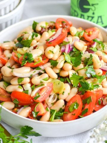 Italian cannellini bean salad in a bowl with a gold spoon in it.
