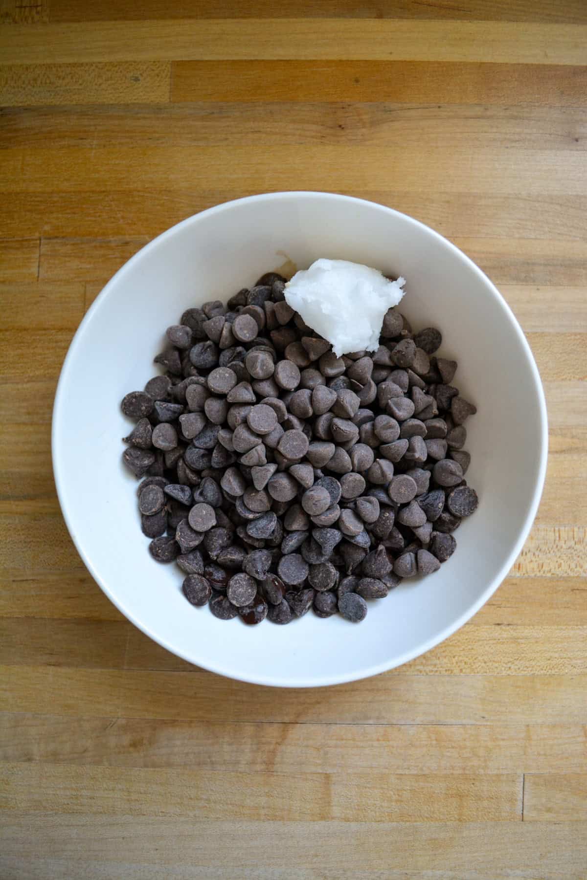 Chocolate chips and coconut oil in a bowl on a wooden surface.