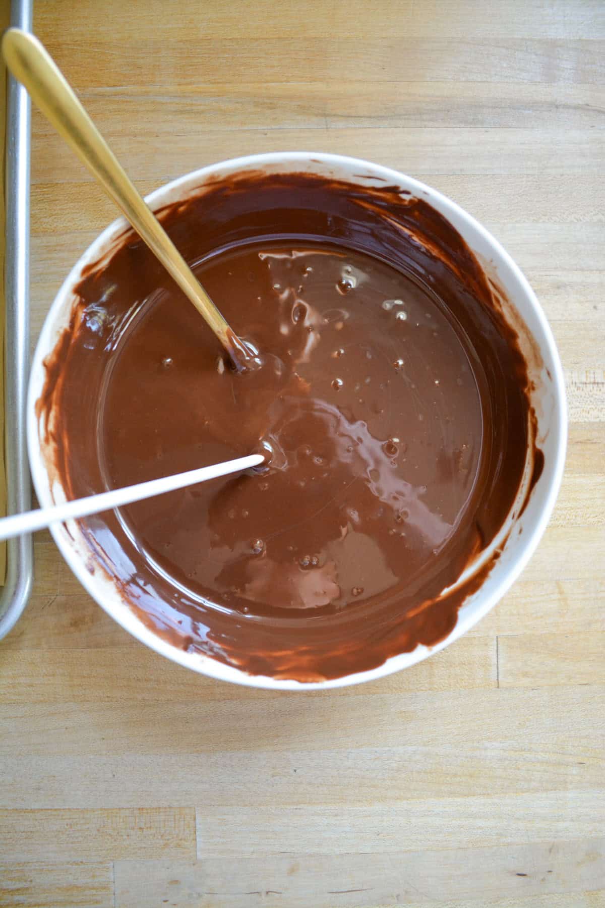Melted chocolate in a bowl with a paper lollipop stick dipped into the chocolate.