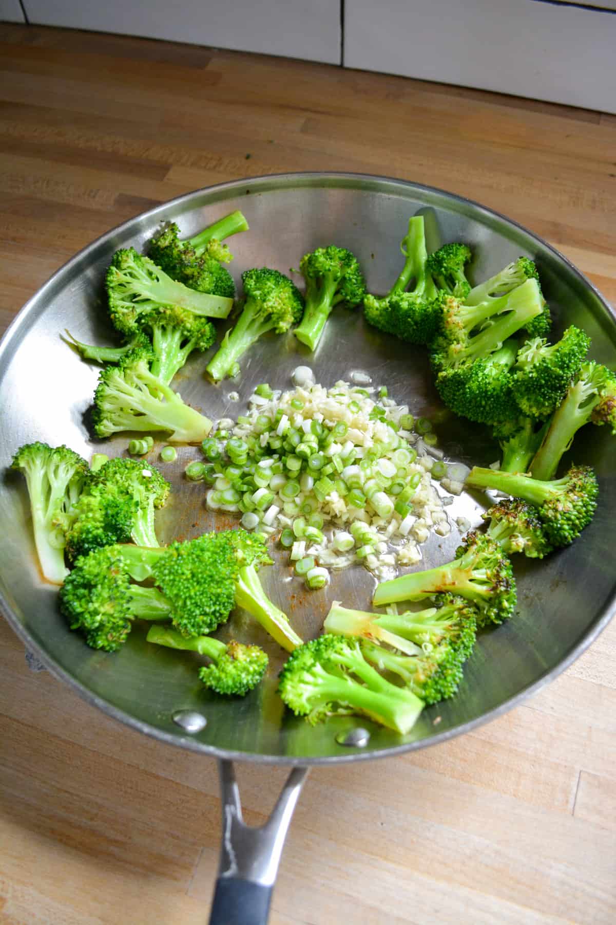 Broccoli florets pushed to the sides of the skillet with chopped garlic, ginger and scallion in the center.