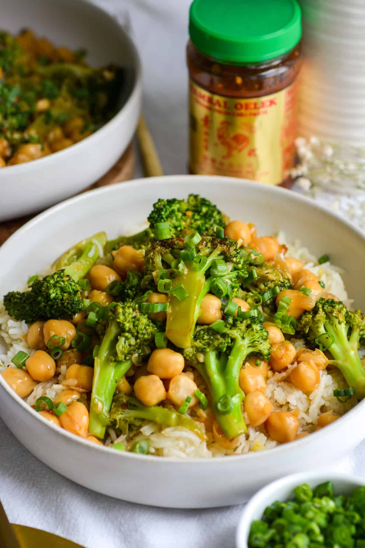 Vegan Chickpea Broccoli Stir Fry in a wide shallow bowl with a container of chili paste in the background.