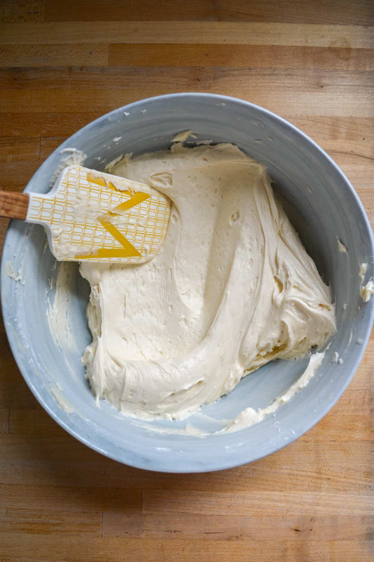 Vegan coconut frosting in a mixing bowl with a rubber spatula in the frosting.