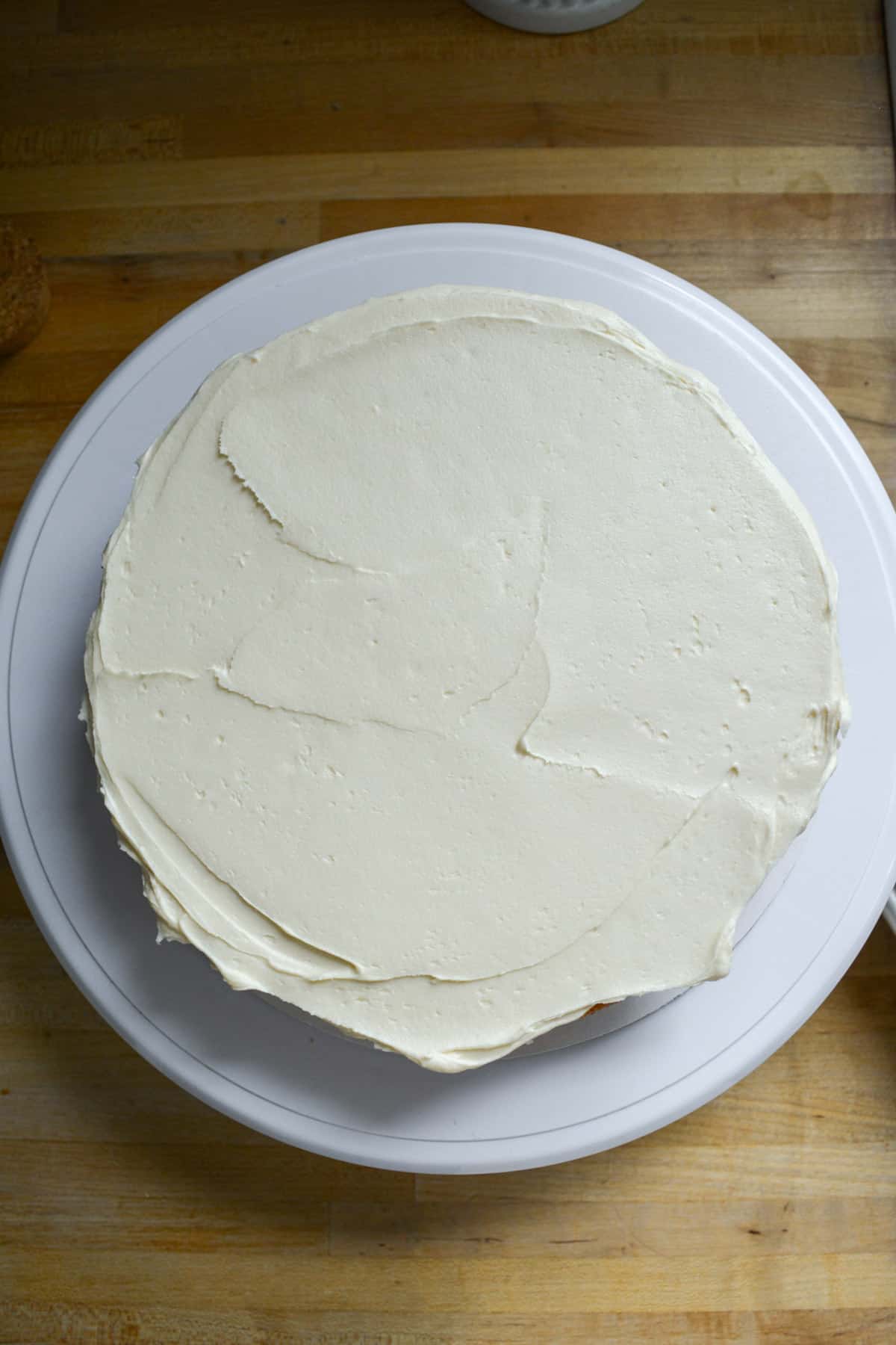 Vegan coconut cake layer on a cake board with frosting spread on it.